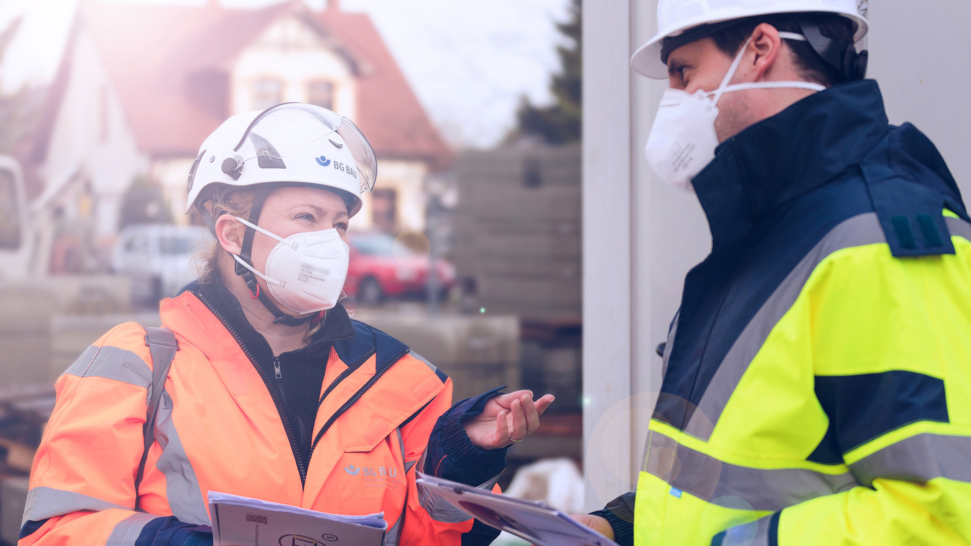 Eine Aufsichtsperson der BG BAU mit FFP2-Maske auf einer Baustelle im Gespräch mit einem Unternehmer